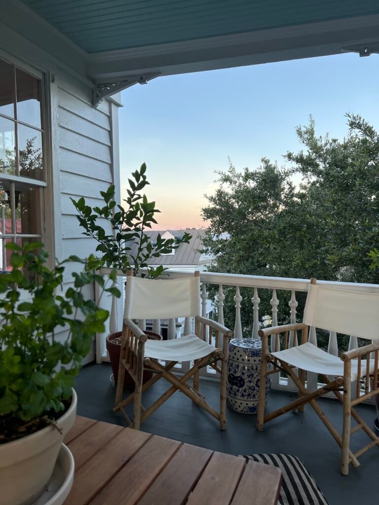 A covered porch with two armchairs and a table at dusk.