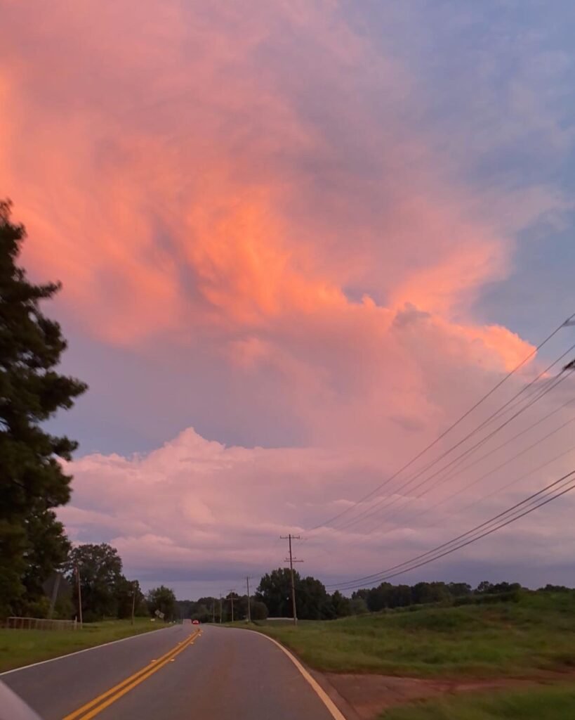 A sunset with pink skies on a two-lane road reminiscent of a sunset you would see at the beach and brings home the feeling of being on vacation.