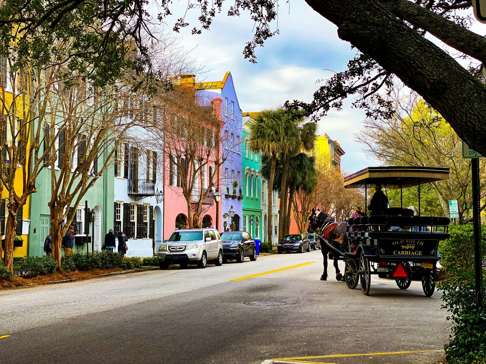 Pastel row houses and palmettos along East Bay Street in Charleston, with a horse-drawn carriage passing