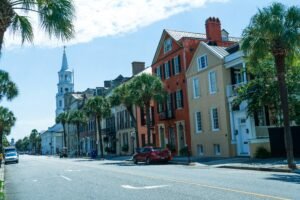 Historic Charleston, South Carolina streetscape with colorful historic homes, palm trees, and a church steeple rising above the downtown skyline.